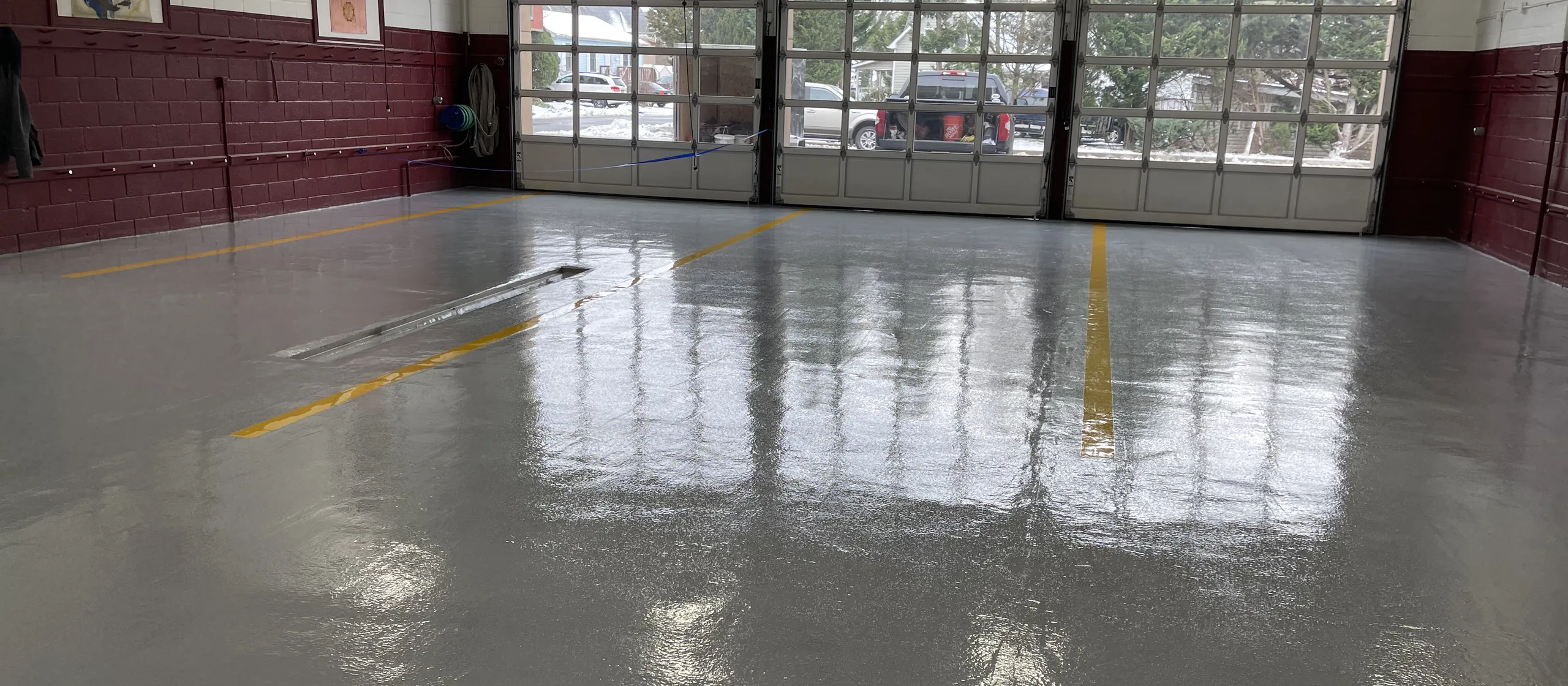 Yellow epoxy striping laid into a grey floor across a fire house apparatus bay