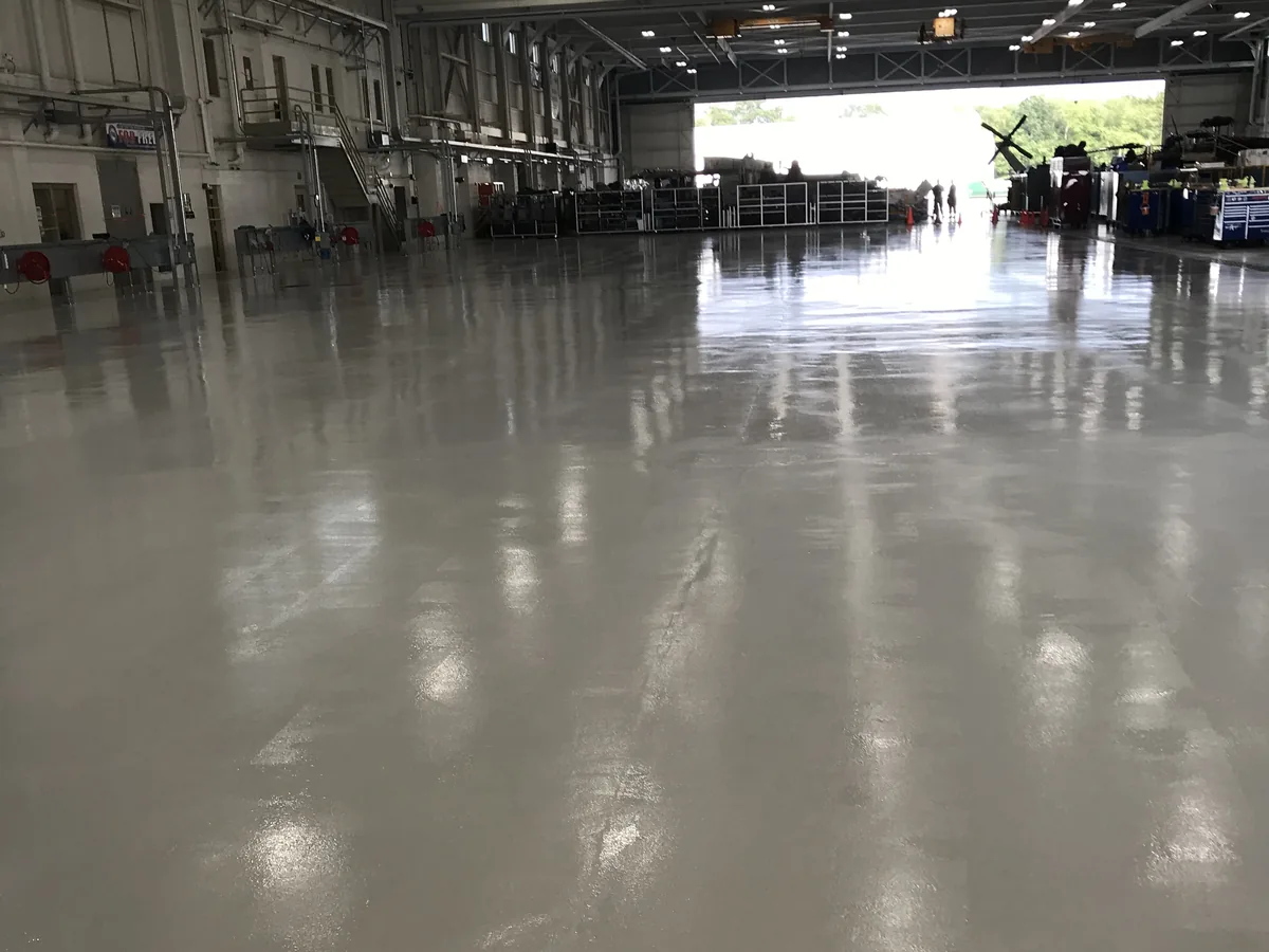 Solid color epoxy floor across an aviation hangar bay, looking toward the open hangar door