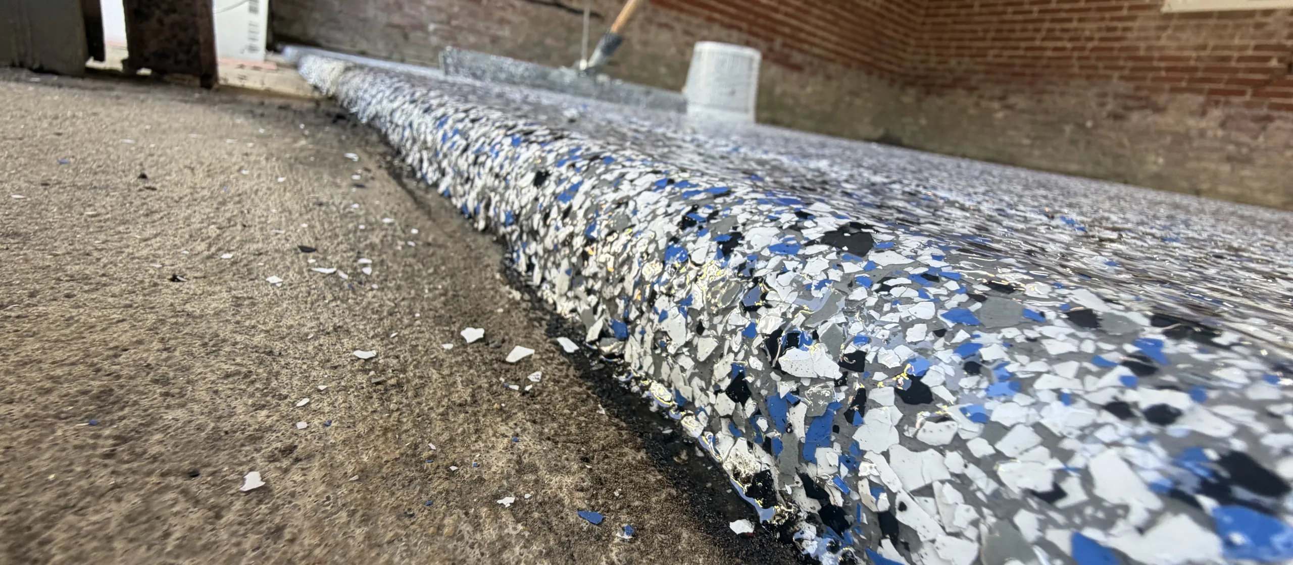 Close view of full-broadcast blue flake epoxy against a brick garage wall