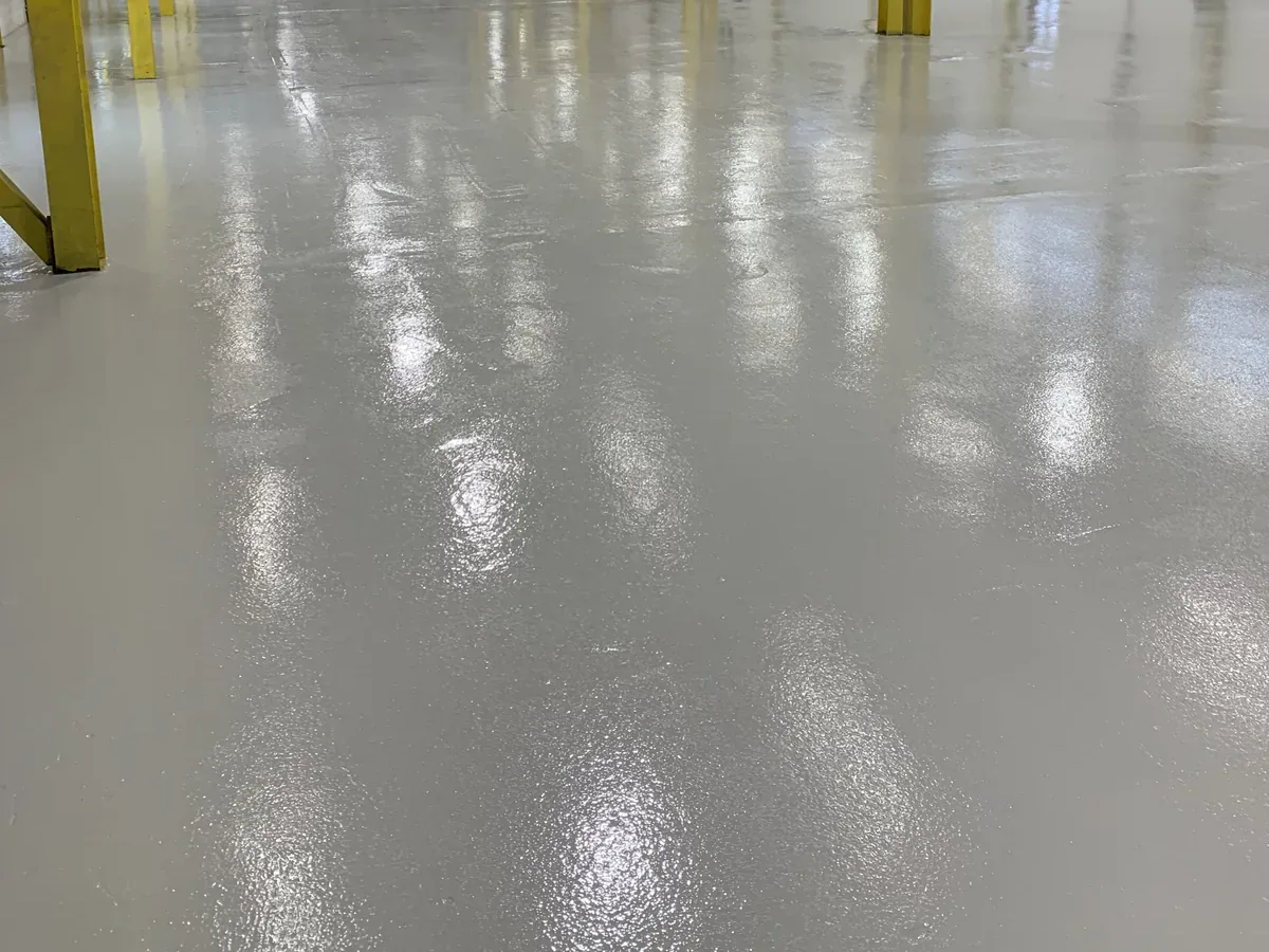 Grey epoxy floor running between the yellow gantry columns of a fabrication bay