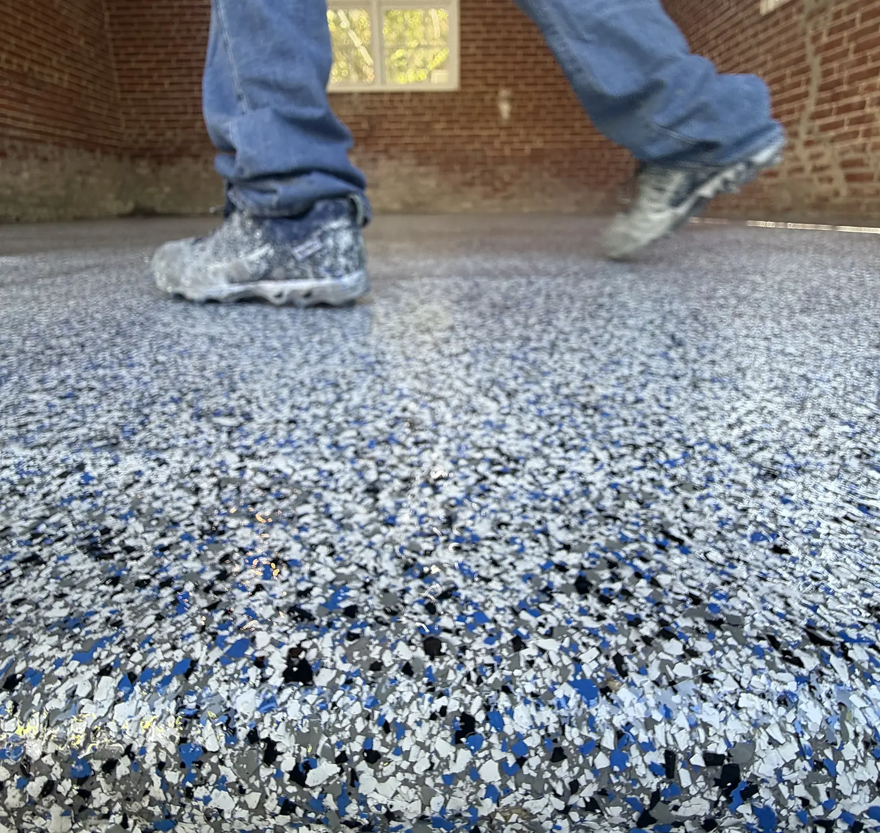 Liberty Epoxy installer in spiked shoes walking fresh blue flake broadcast in a Philadelphia garage
